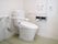 共用トイレは広いスペースに設置されている。トイレットペーパーホルダーの上に、L字型の手すりが付けられている
