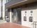 玄関扉の横に、看板とインターホン、郵便受けが２組取り付けられている。郵便受けの近くに手すりがある。
