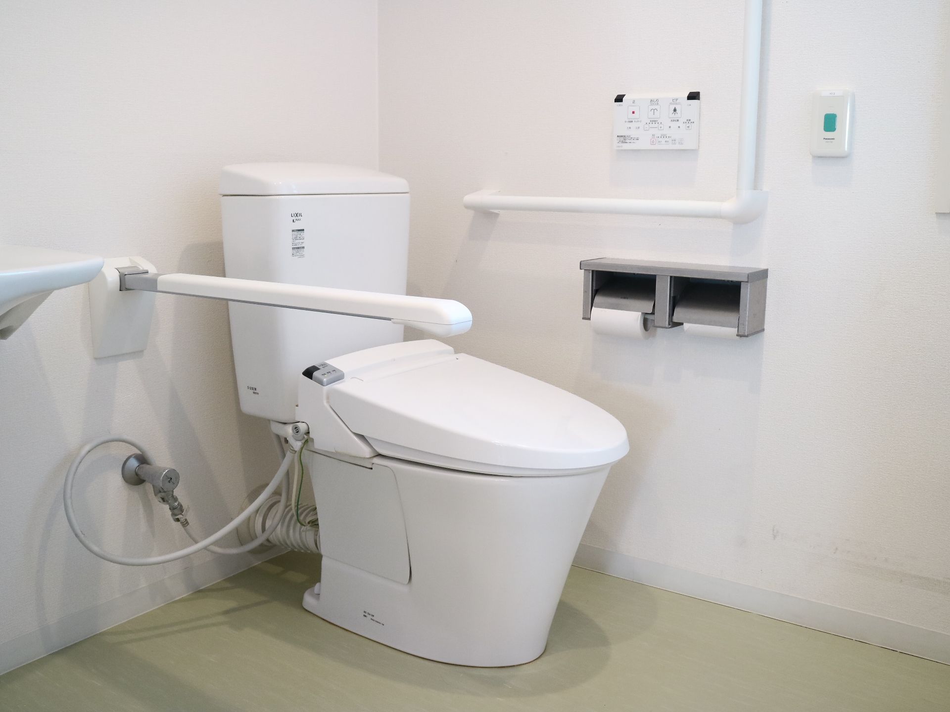 白い壁にL字型手すりやレバー式手すりが設置されたトイレ空間