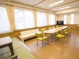 黄色い椅子がセットされた大きなダイニングテーブルやソファ、和のスペースがある共有部。