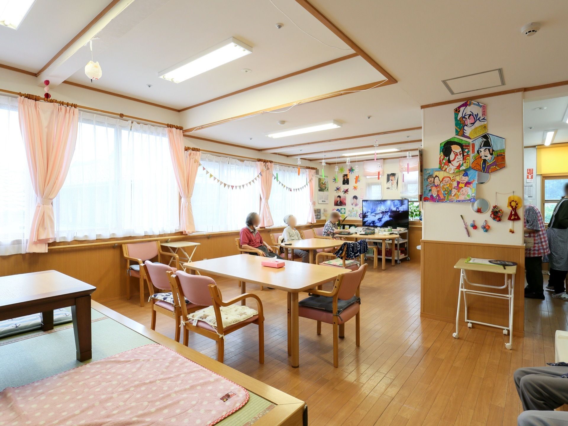 共有スペースにはテレビが置かれ、座って見ることができる。カーテンや椅子の背もたれ、座布団カバーがピンク色で統一されている。