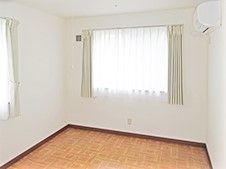 ワンルームの小さな部屋の一角。何も置いていない空き部屋の窓を写した写真。隅のほうにエアコン