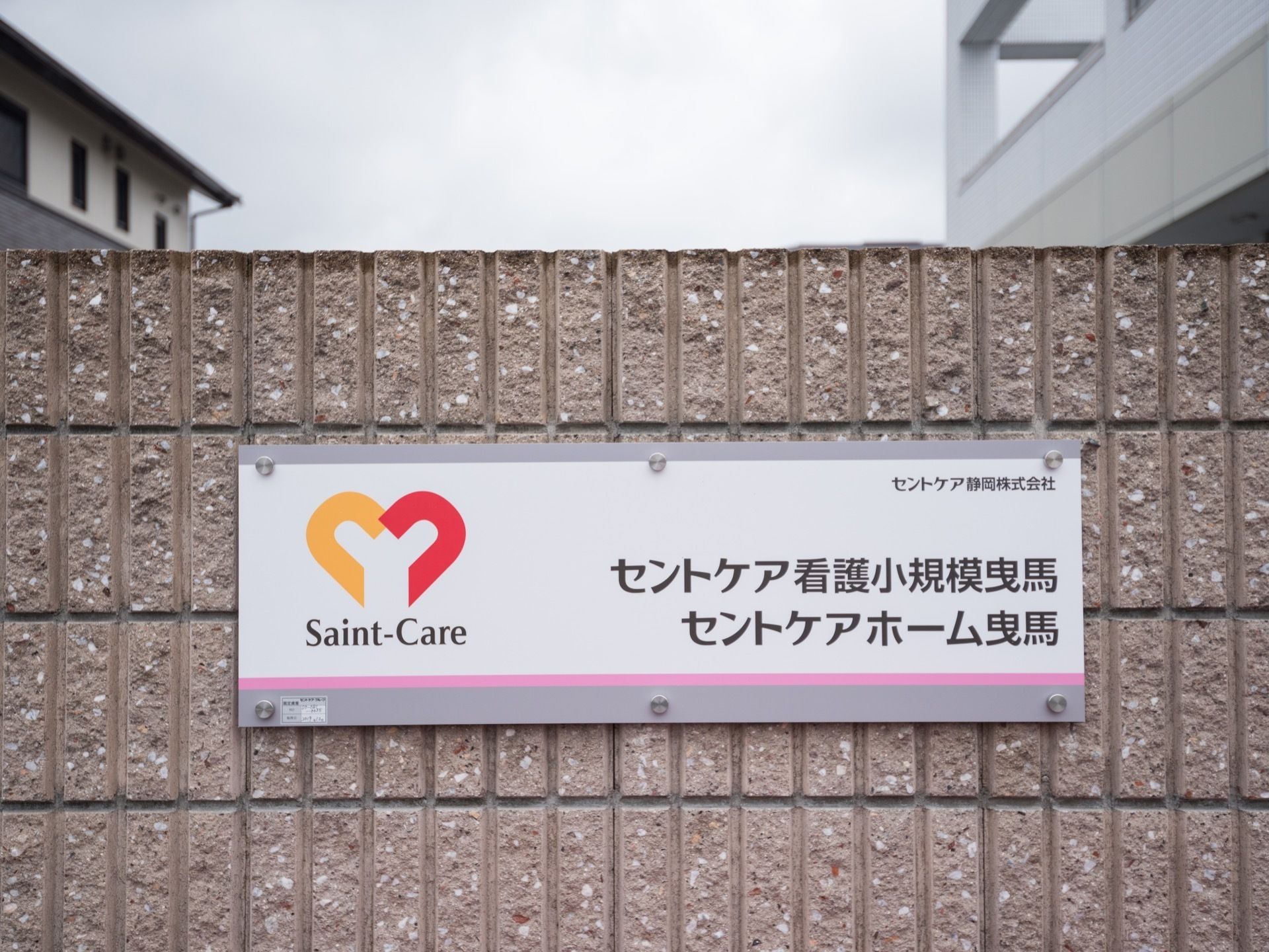 施設外壁に表札が取りつけられている。四角いパネルの右側には施設名が、左側にはシンボルのマークが書かれている。