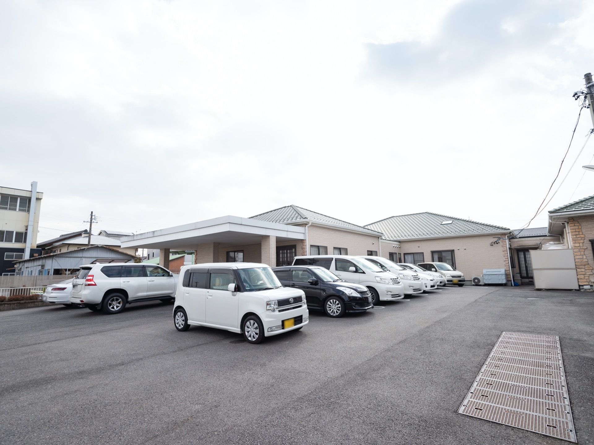 やさしい色調で施工された平屋建て施設の周囲には、駐車場スペースが設けられている。複数台の乗用車が停車している。