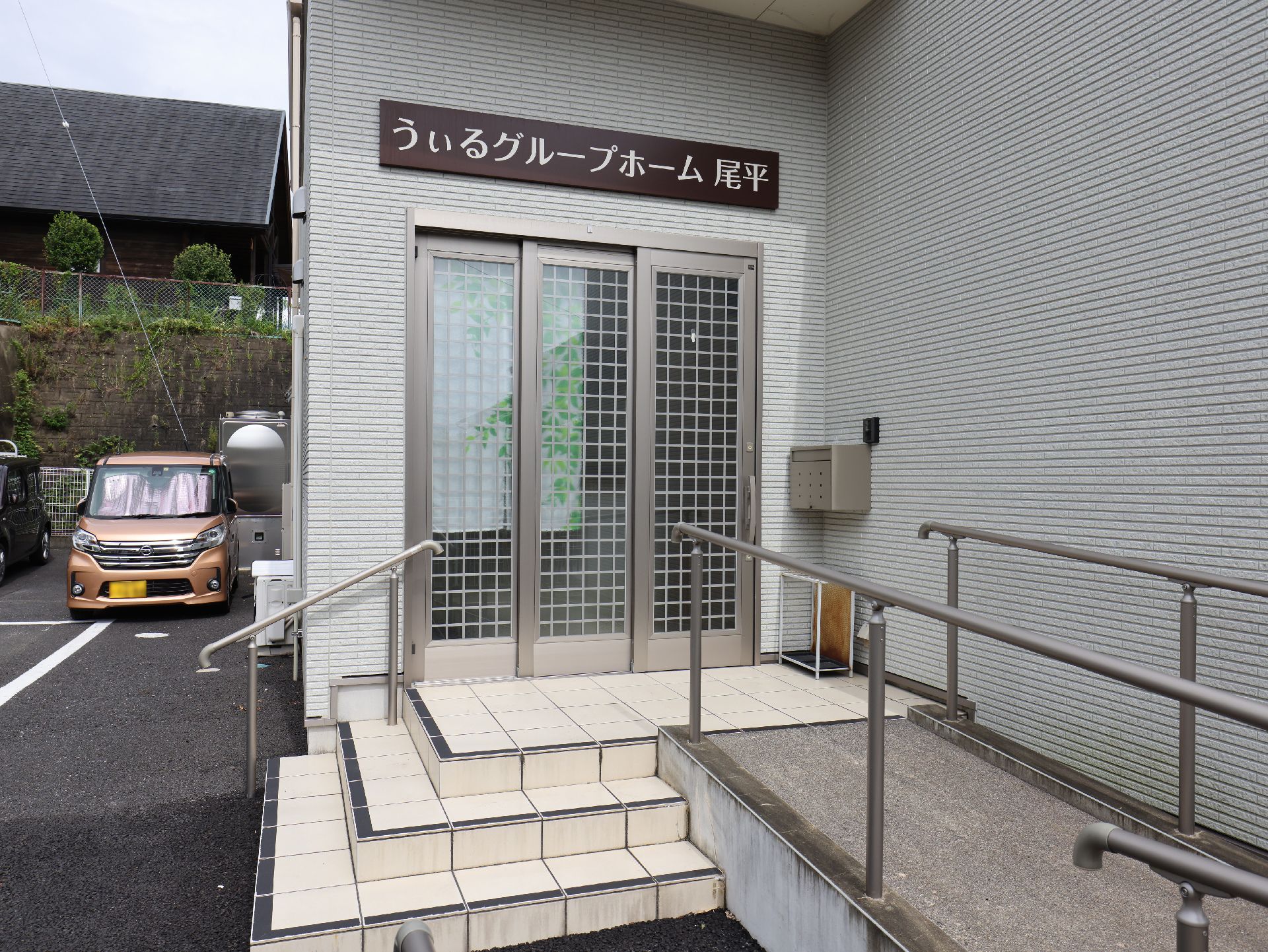 白い壁の建物の入り口についた手すり付きの階段とスロープ