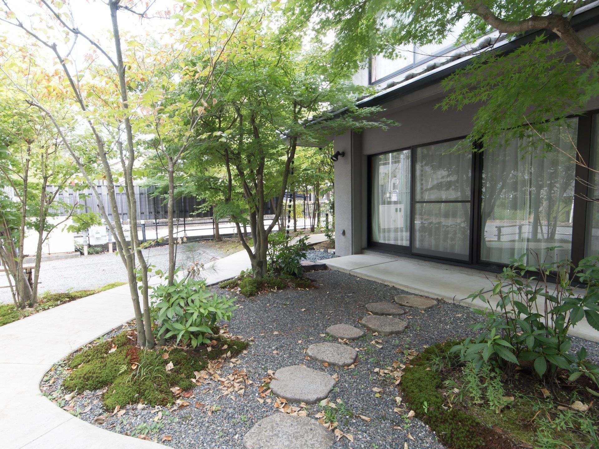 建物の前に、砂利に飛び石を設置した中庭がある。高木の足元に苔を生やしたものを所々に植えられている。舗装された散策路がある。