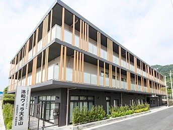 3階建ての建物はモダンなデザインで周りにはたくさんの緑がある。ホーム名が書かれた看板も立っている。