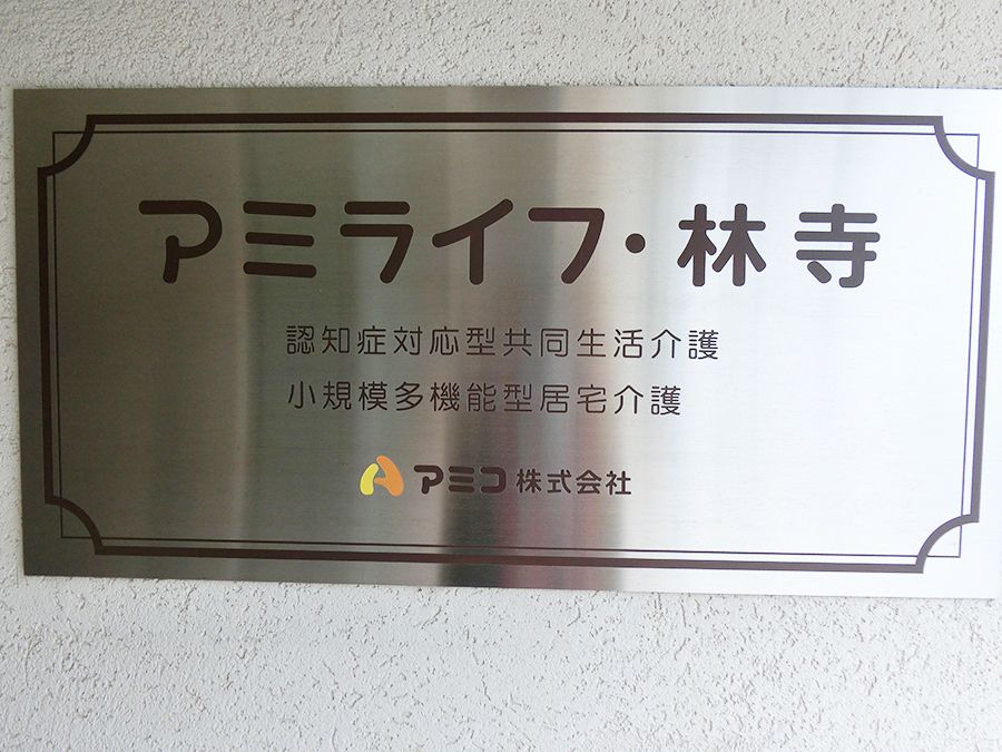 シルバーのプレートがグレーの外壁の建物に貼られている。プレートには黒い文字で事業所名が書かれている。
