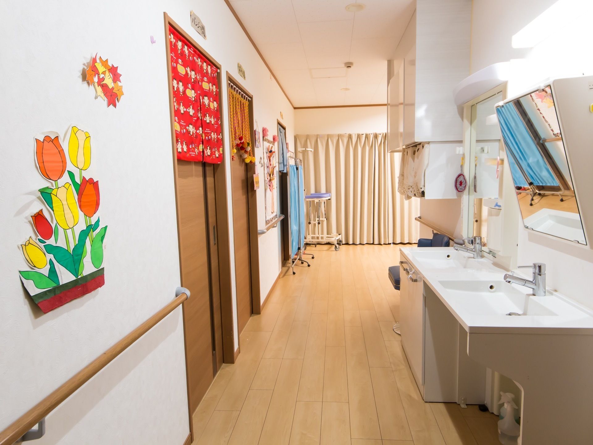 壁にはチューリップのイラストが飾られていて、その下には手すりがある。部屋の扉の前には洗面台が設置されている。
