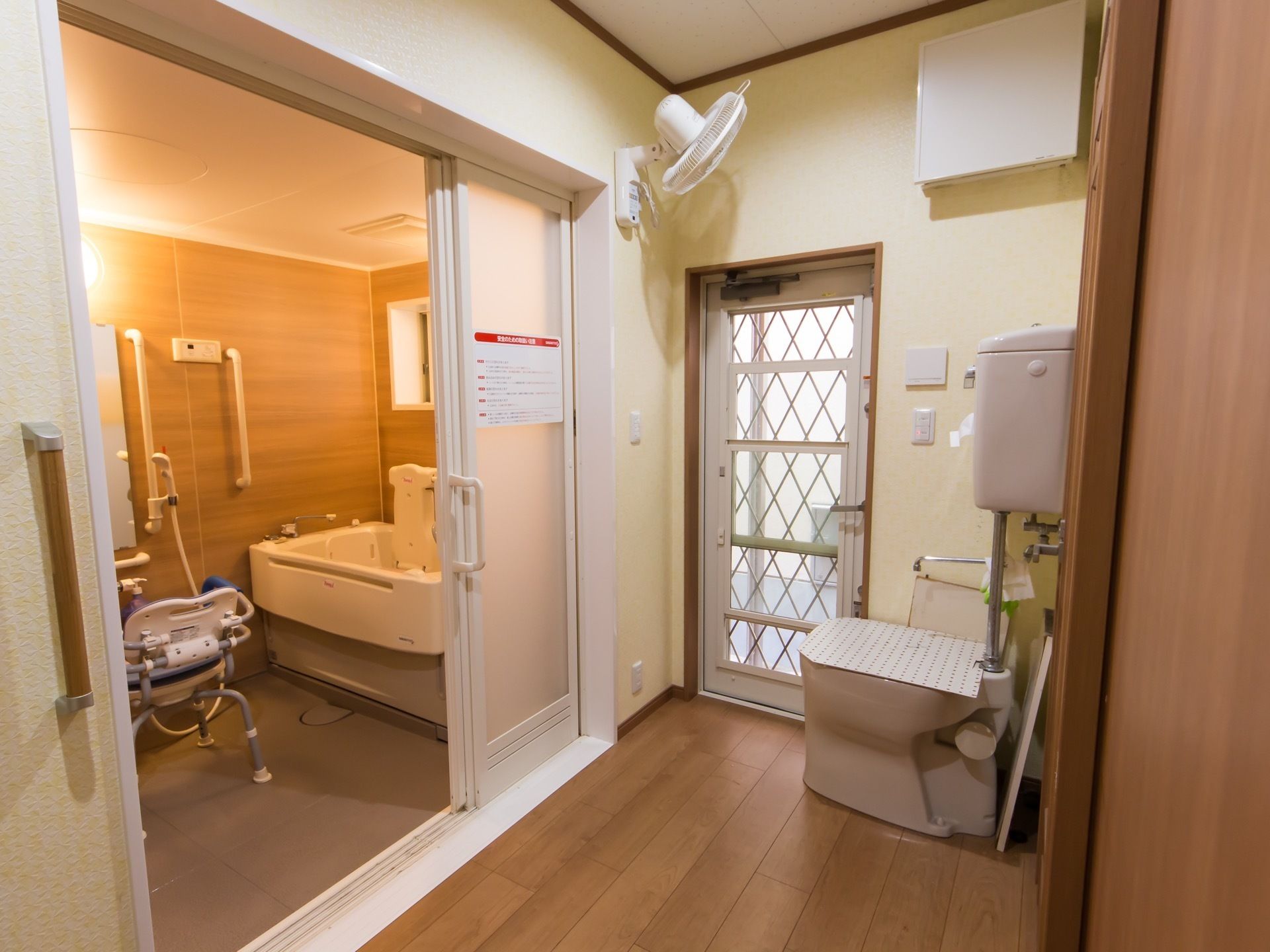 脱衣所にはトイレが設置されており、トイレに向けられた扇風機もある。浴室の扉は開いていて、浴槽と洗い場が見える。