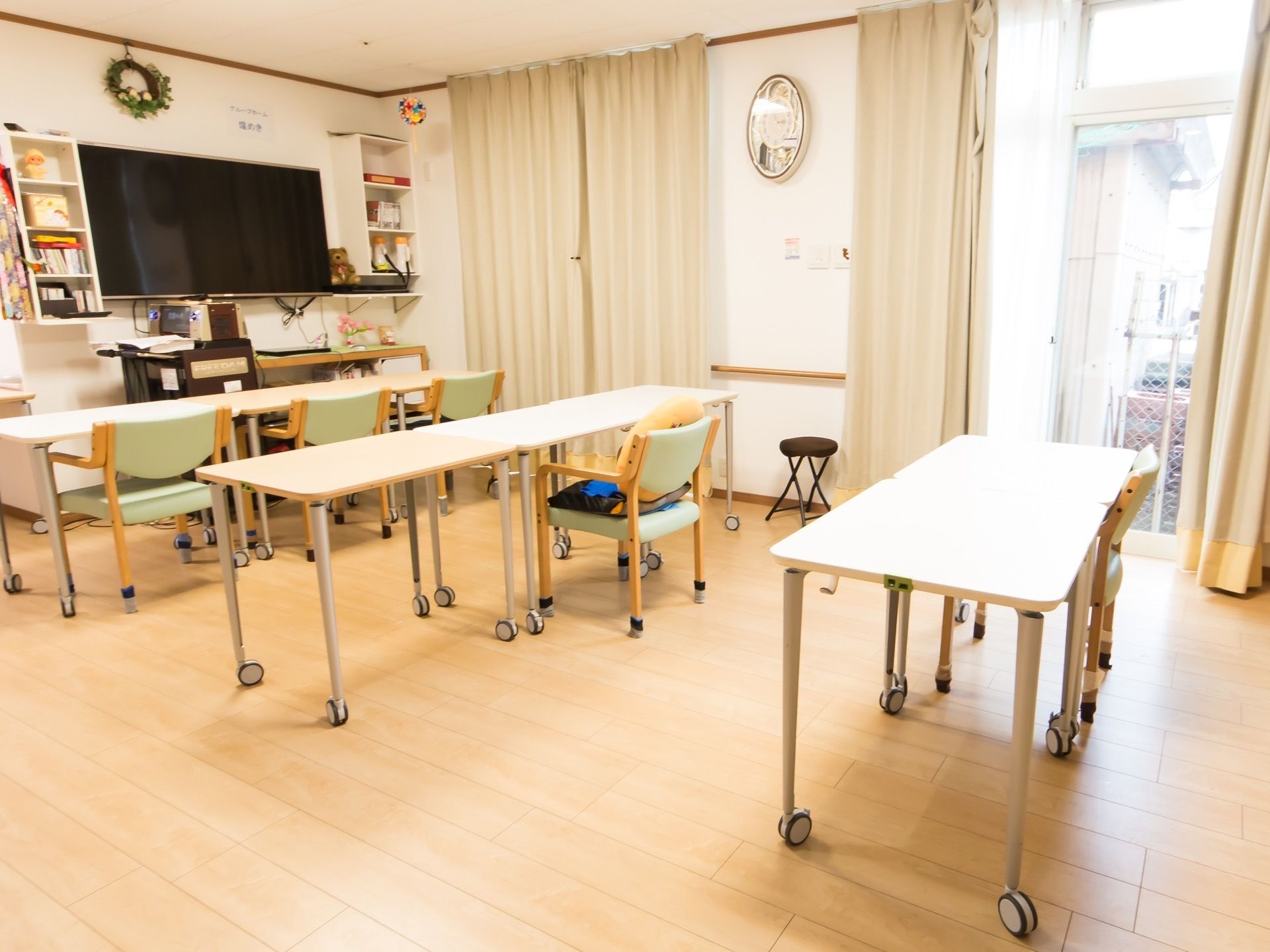 大きなテレビが設置されている両側には壁掛けラックがある。テレビ正面にはテーブルと椅子がある。
