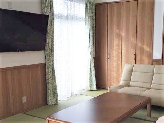 畳敷きのリビングにはベージュのソファと長テーブルが置かれ、大きな壁掛けテレビがある。