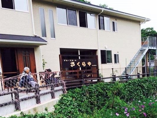 2階建てのベージュを基調にした建物。玄関には屋根が付き、屋外階段もある。