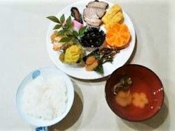複数の種類のおかずが盛られたお皿の横には白いご飯と汁物がある。