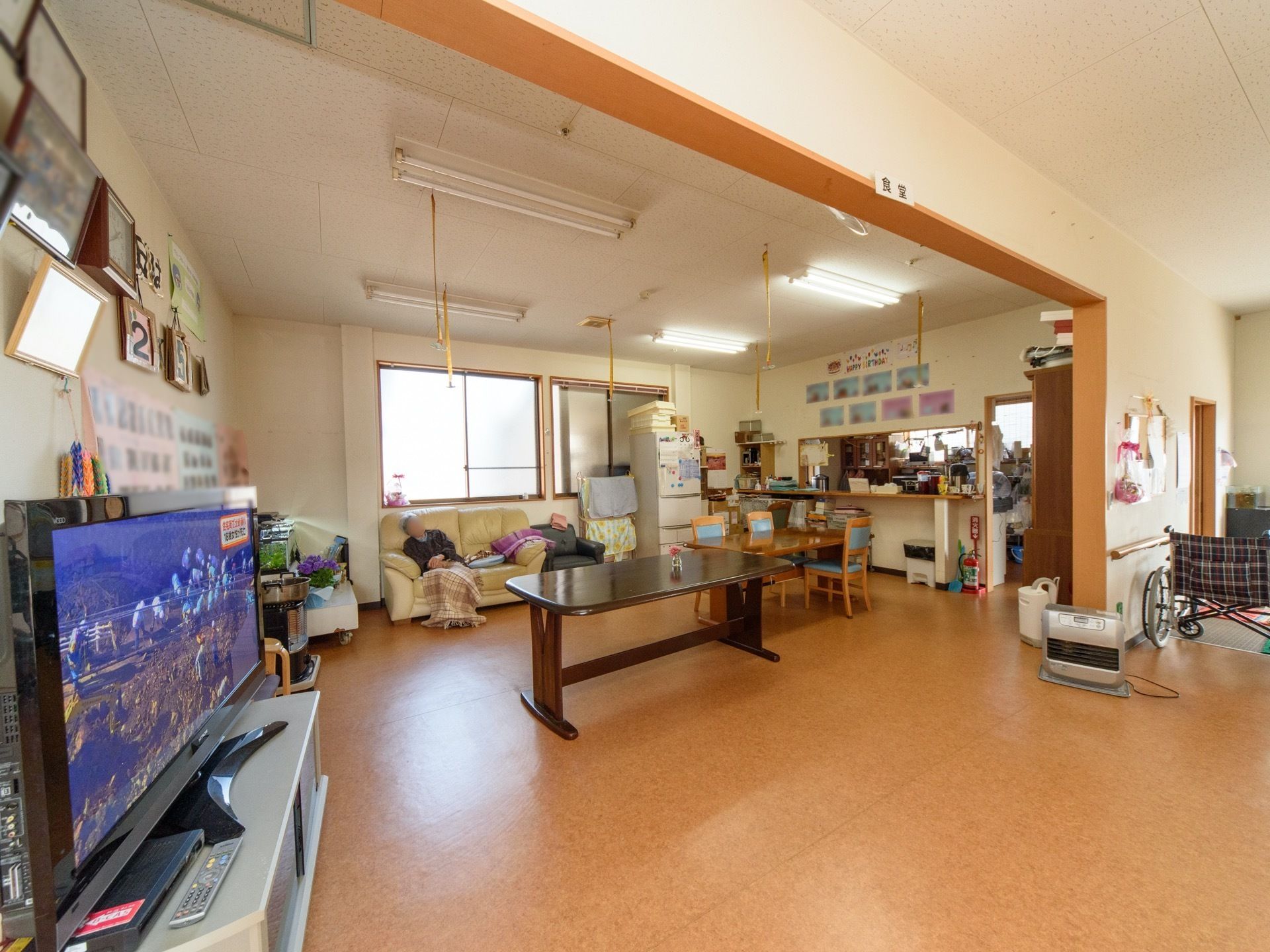 食堂にはテレビが設置されている。入居者様の作品や写真などが飾られている。キッチンがそばにあり、スタッフとの距離が近い。