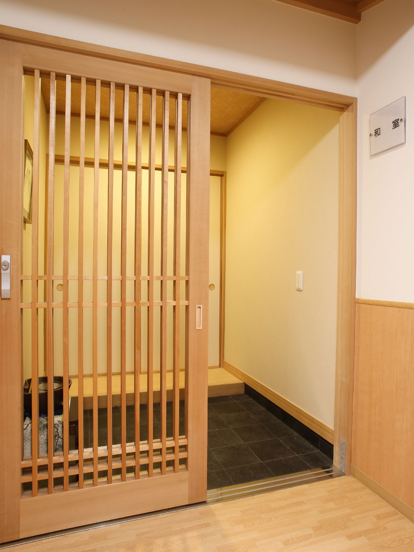 共用施設の和室の入口。和室と書かれたプレートや、扉、照明、飾られた絵など、旅館の一室のような雰囲気がある。