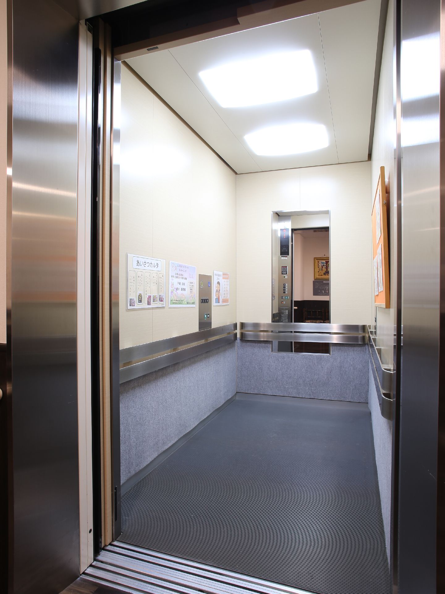 ベッドのまま移動できる、奥行きのあるエレベーター。壁には手すりを設置。奥には鏡、壁にはお知らせなどを掲示している。