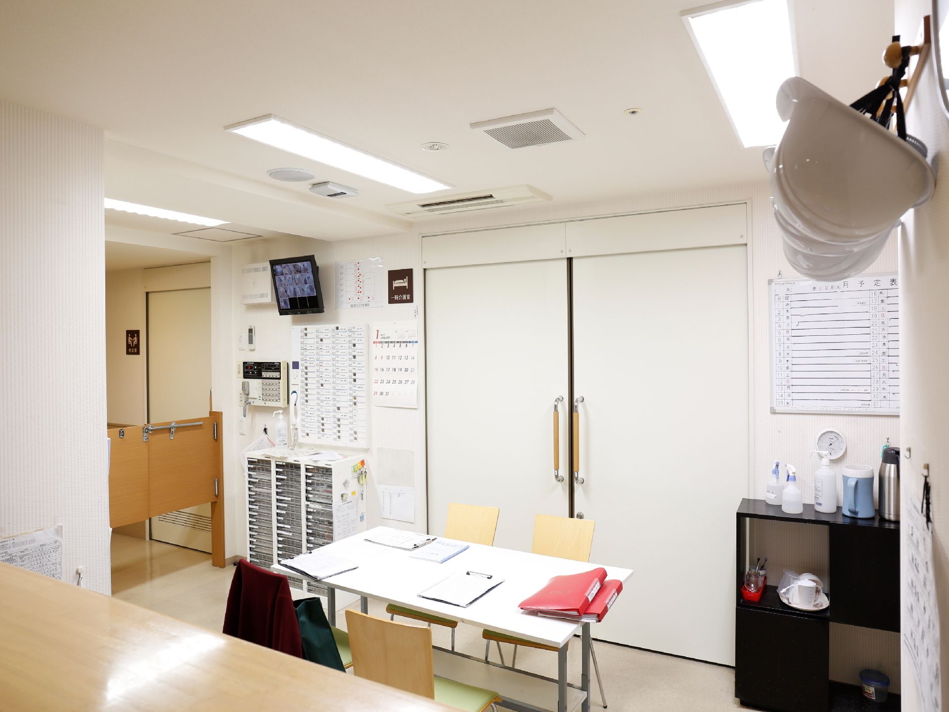 建物内の入居者用、来客用の施設と違い職員のスペースは非常に簡素な作り。施設内の様子をモニター可能で、防災ヘルメットも設置されている。