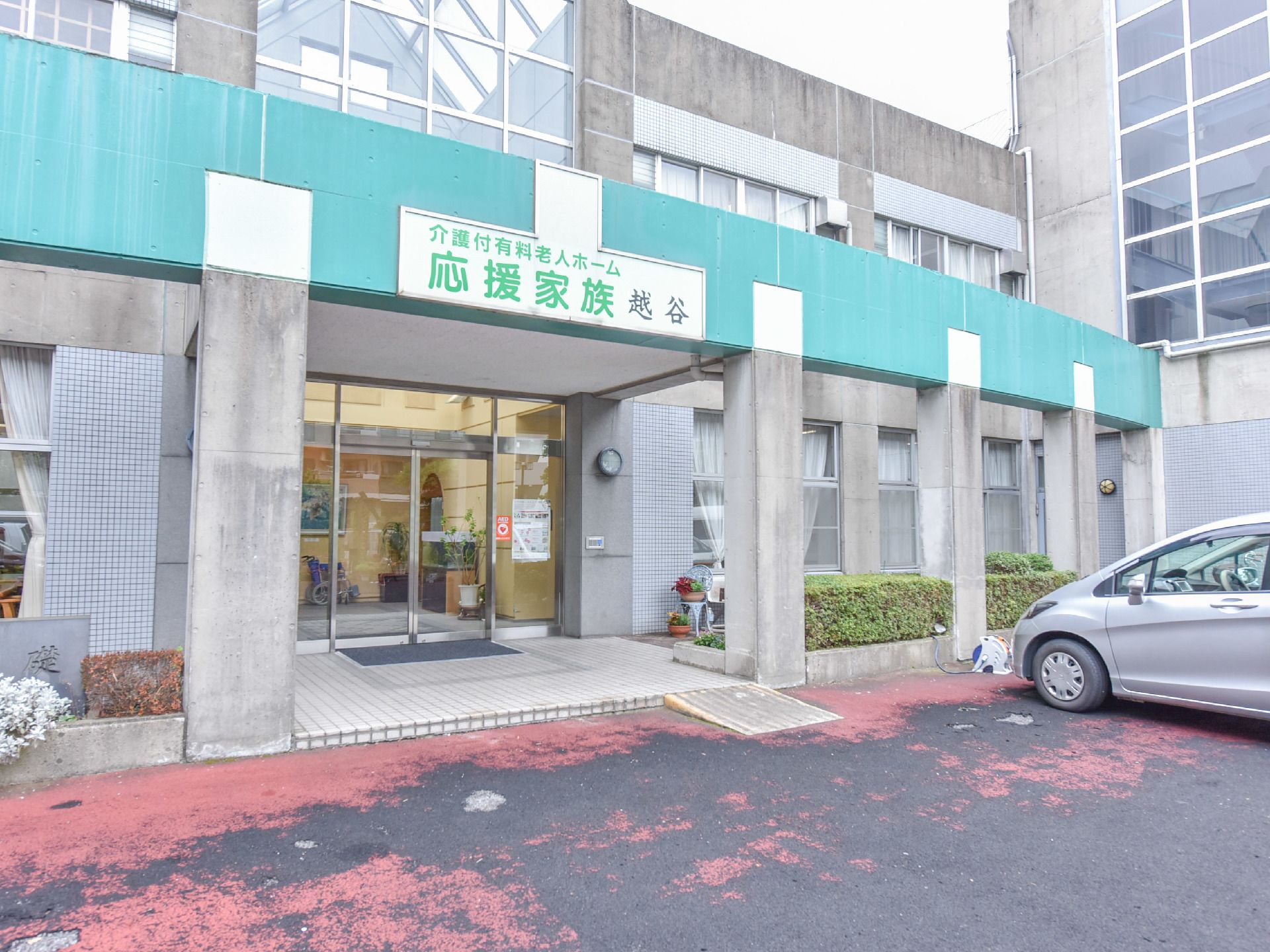 入り口の頭上には施設名の入った看板がでており、ガラス張りで両開きの自動ドアの玄関までは雨よけになっている。