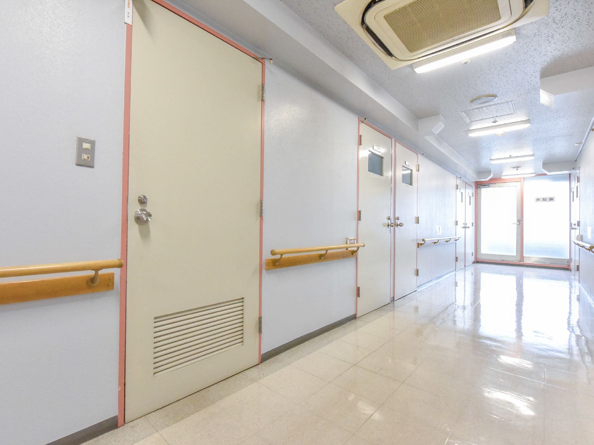 突き当たりはガラスの扉になっており明るい光がさしこんでいる。空調のついたろうかには大きな扉と手すりが敷設されている。
