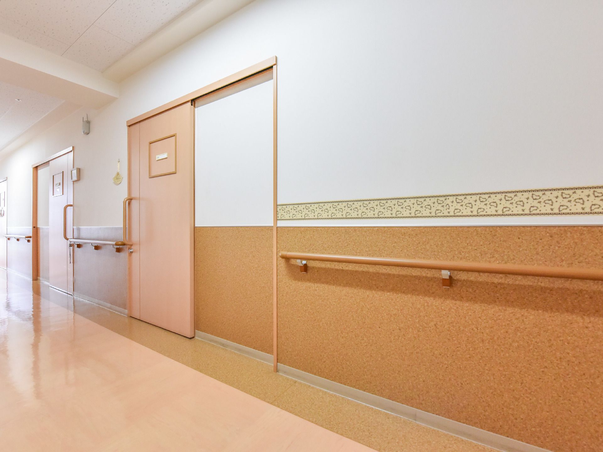 段差のない廊下である。ハンドルドアでスライド開閉の扉がついた部屋が並んでいる。壁には手すりがついている。