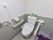 左右に手すりがついたトイレである。シートの横にウォシュレット用の操作パネルがある。貯水タンクに、予備のトイレットペーパーがある。