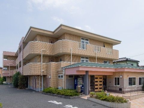 入口横に自動販売機が設置されている、ベージュの外壁で落ち着いた色合いの施設の外観