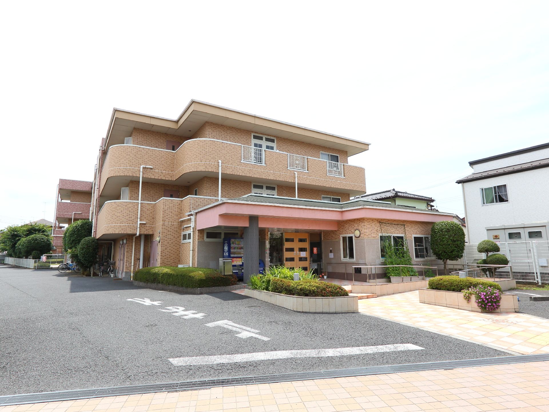 白いフェンスで施設は囲まれている。木々が多く植えてある。スロープがあり、花壇が両サイドにある。手すりがついている。