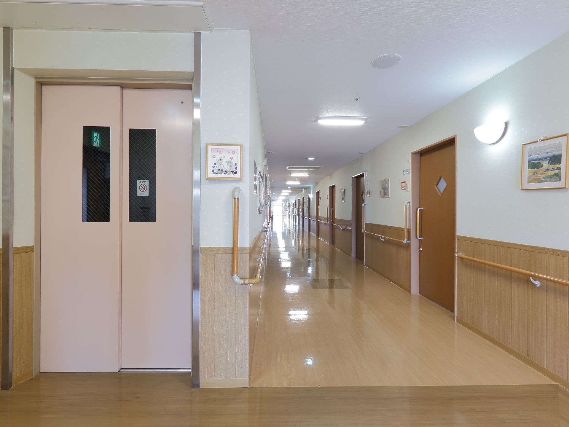 施設の廊下の突き当たりはエレベーターホールになっている。ホールにも手すりがあり、ピンク色のエレベーターが設置されている。