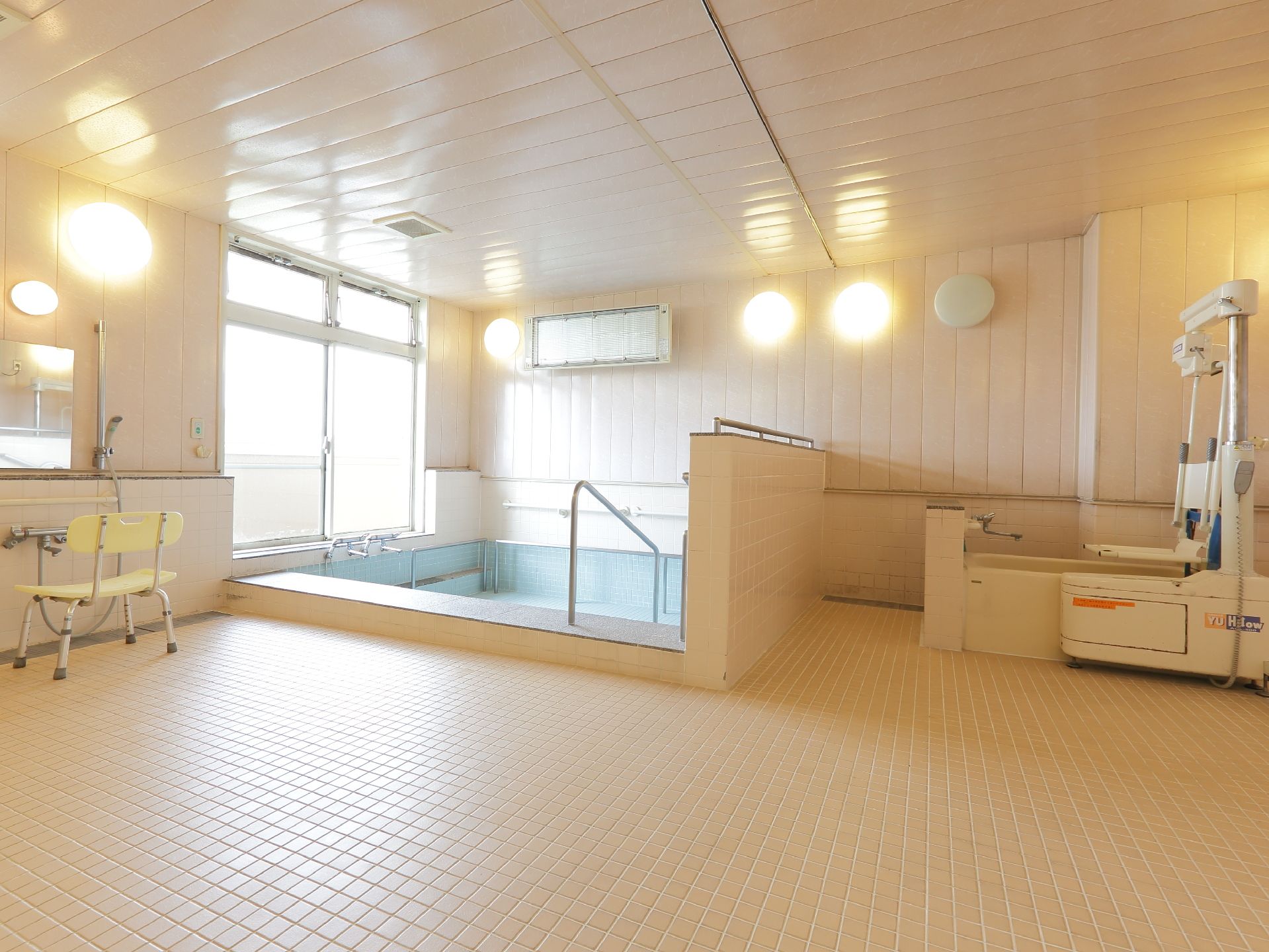 左にサーモスタット式シャワーがついている。バス用チェアがある。湯船そばに窓がある。手すりがついている。