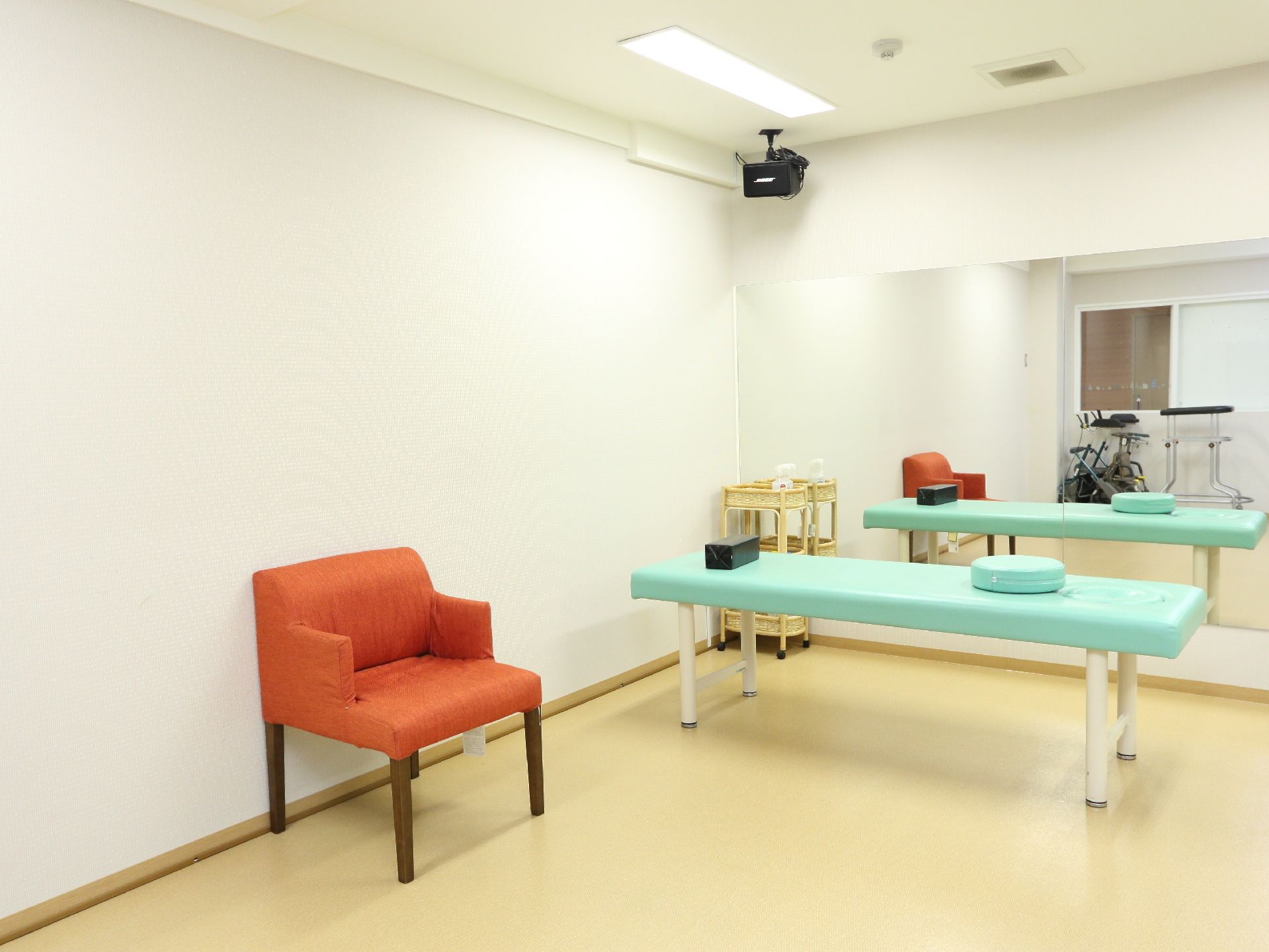 バリアフリーの部屋である。壁が白い。オレンジ色の椅子がある。簡易ベッドが置いてある。