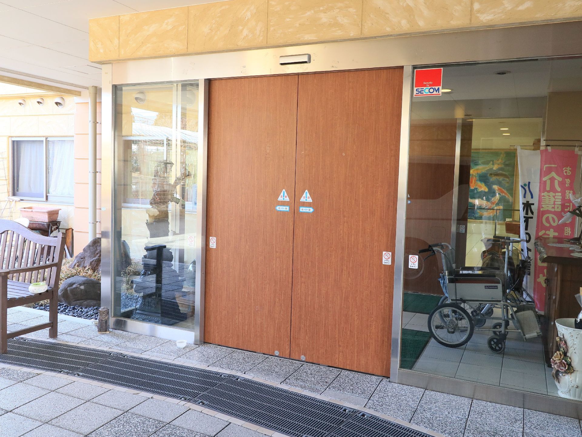 スッキリとした広いエントランスである。出入口の扉には、木目調の自動ドアが設置されている。木製ベンチが置かれている。