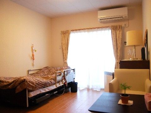 ベッドサイドには緊急通報装置があり、エアコンや寝具付きのベッドが置かれた部屋にはソファやテーブルもある。