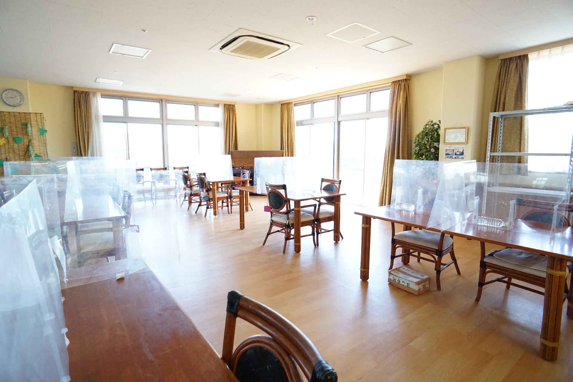 壁２面に窓ガラスが配置された透明な仕切りが付いた木製の机が並んだ広間