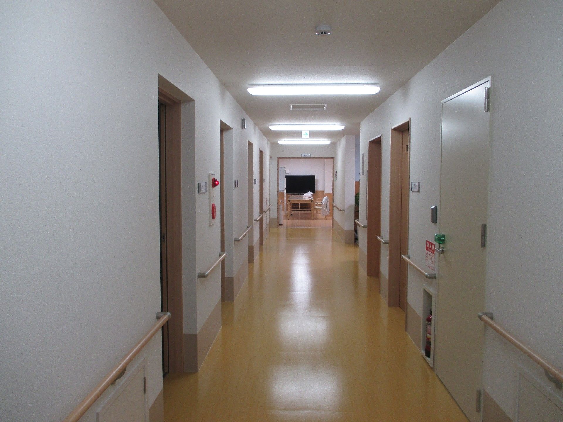 壁に手すりが設置され、非常ベルや消火器が備え付けられた居室前の廊下
