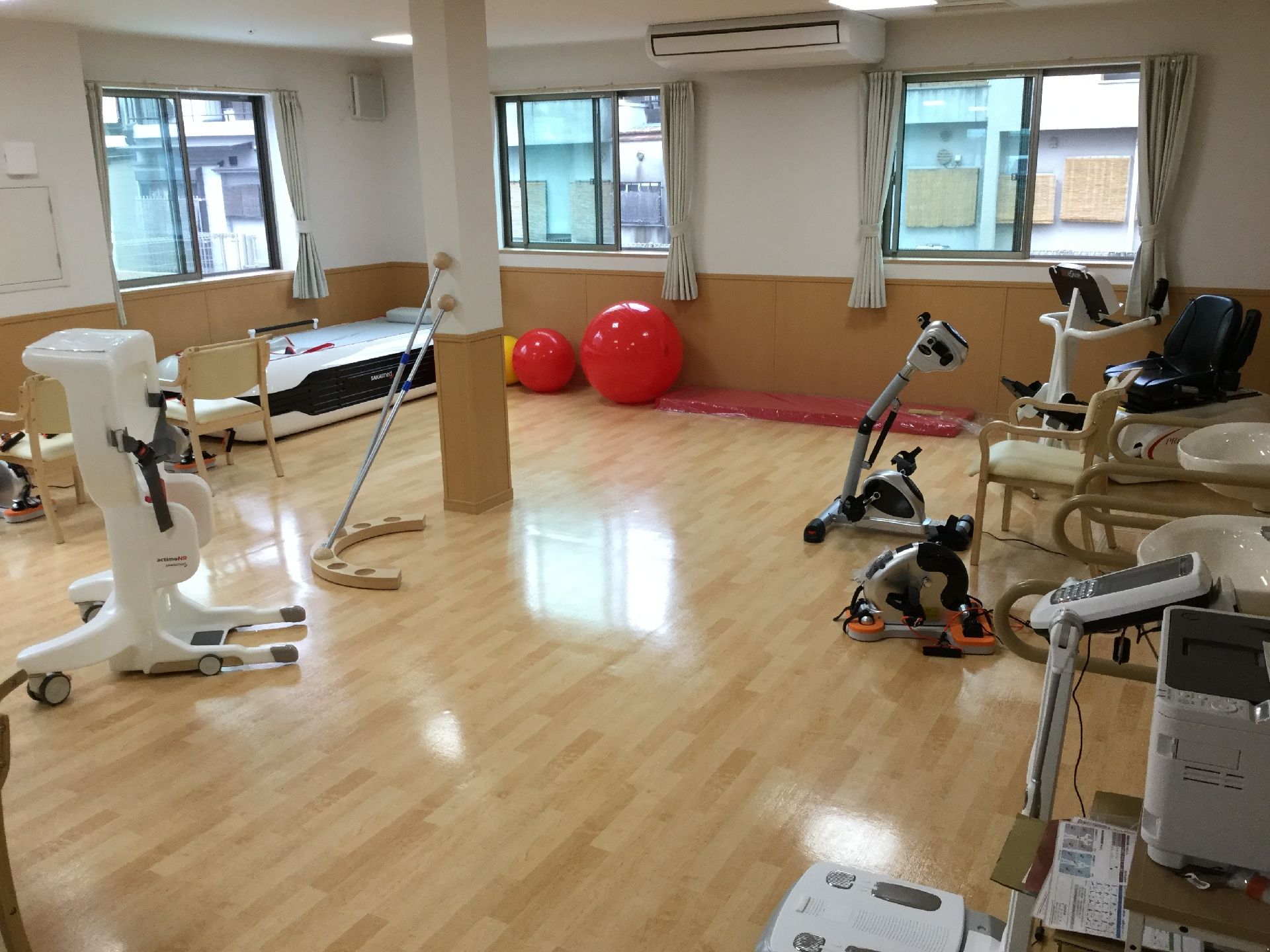 バランスボールをはじめとした機能訓練に役立つ道具が置かれている部屋。窓が３つあり、いずれも開いている。