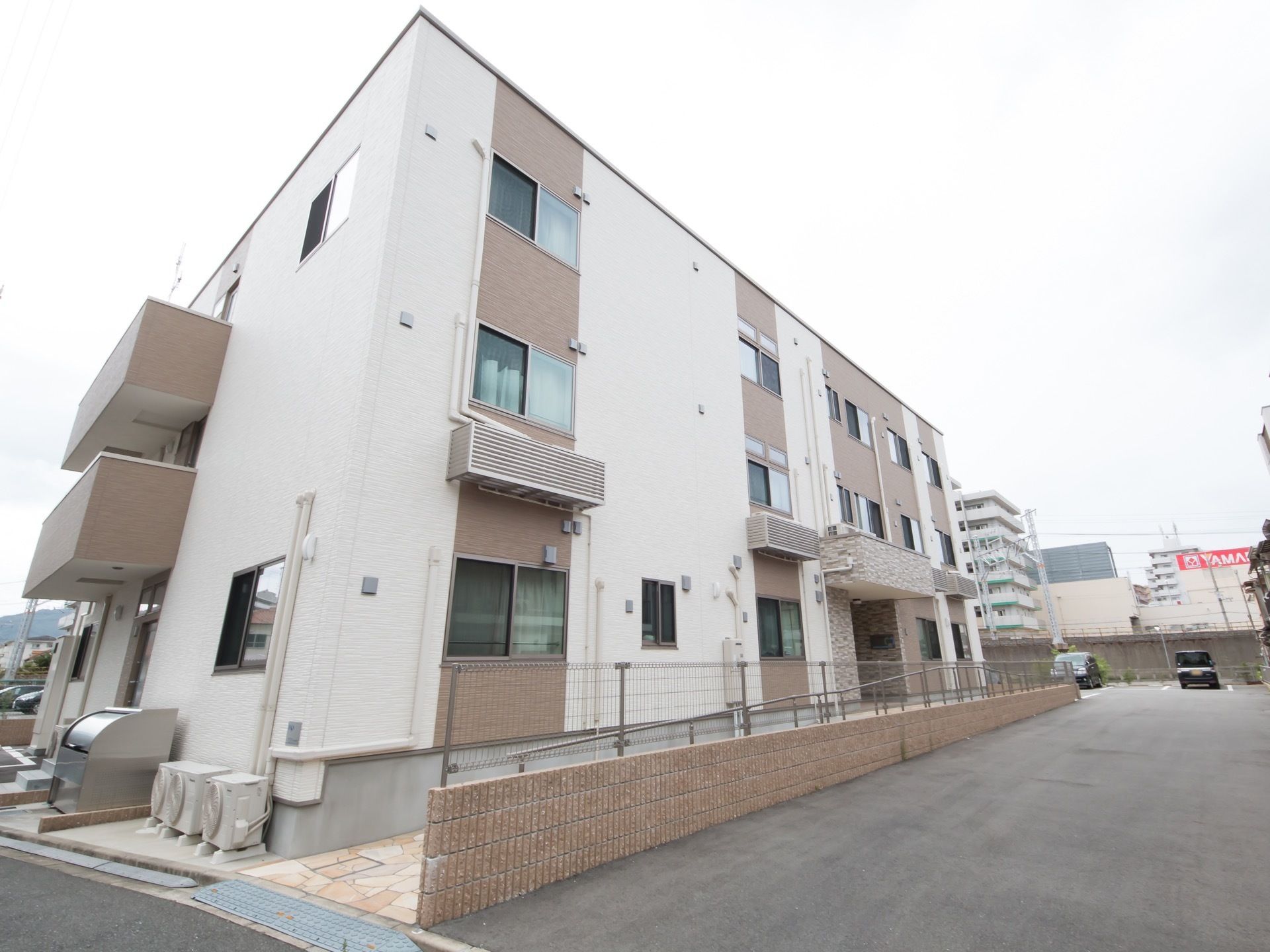 白色の壁に茶色のレンガの入った、３階建ての建物である。駐車場と歩行者用のスロープの間にはフェンスが設置されている。
