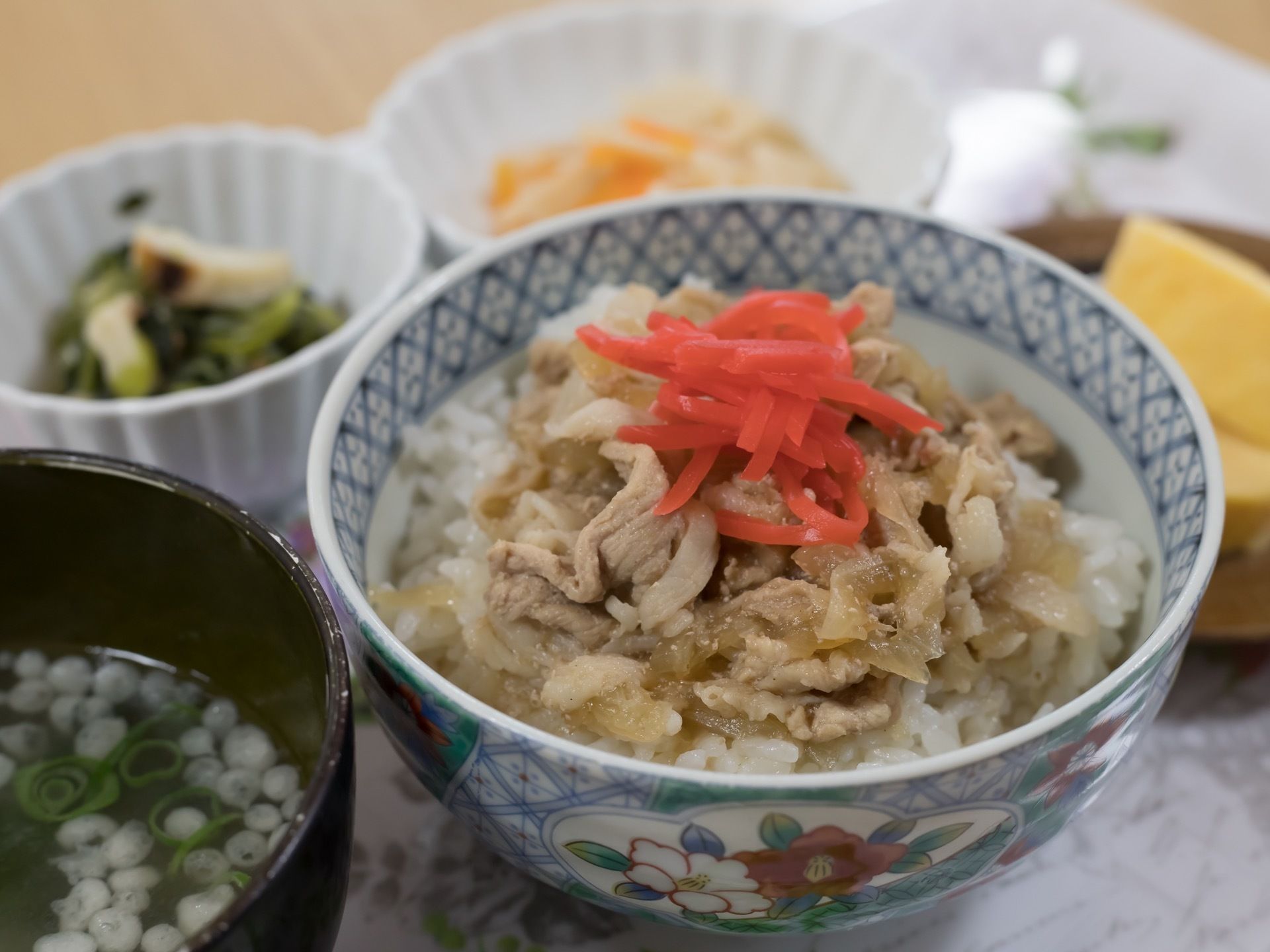 お盆に食事の支度がされている。メインは牛丼で、すまし汁や複数の副菜の小皿も周りに載っているのが見えている。
