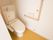 トイレの壁に、L字型の手すりと緊急ブザーが設置されている。トイレは自動洗浄機能付きで、個室の扉は引き戸である。