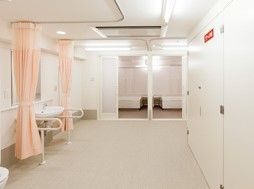 床と壁一面が白に統一されており、仕切り用のカーテンはピンク色である。洗面台には手すりが設置されている。
