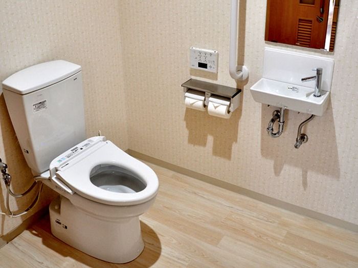広く清潔感のあるトイレ。トイレの中には手洗器と鏡が設置されており、その隣には手すりが備え付けられている。