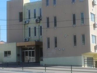 広い道路に面した建物である。玄関には屋根が付いており、入口はガラス張りとなっている。横の外壁にはポストが設置されている。
