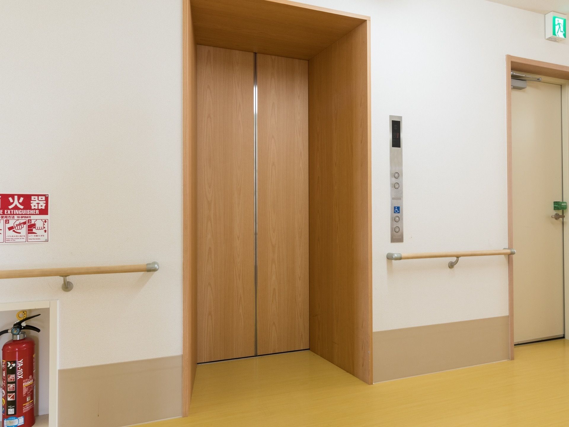 温かみを感じる木目調のエレベーターである。ホール周辺は、手すりや防災対策として消火器を完備している。