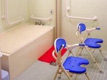 浴槽のそばに赤い滑り止めマットが設置され、洗い場に２脚のバスチェアが置かれた浴室