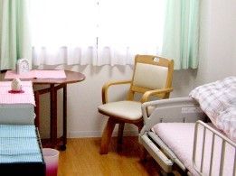 窓のそばに一人用のテーブルセットが置かれ、介護用ベッドが設置された居室