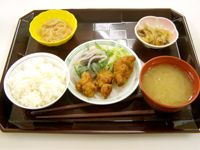 茶色いトレイにご飯とみそ汁、揚げ物と野菜が盛り付けられたお皿が置かれており、２種類の副菜も用意されている。