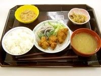 黒い配膳盆の上に、揚げ物に野菜が添えられたおかずを中心に、白米やみそ汁や小鉢が並べられ、箸が１膳置いてある。
