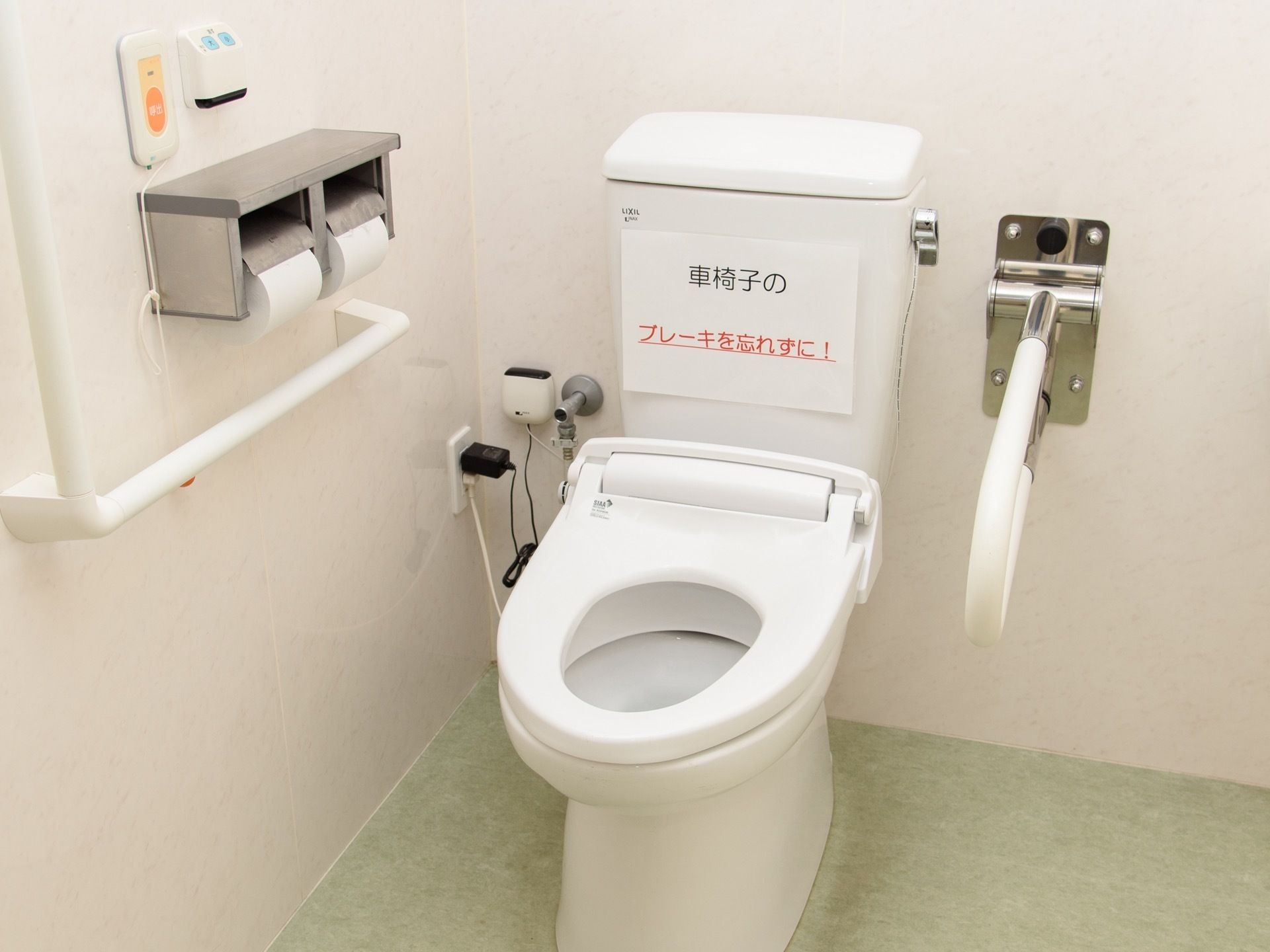 タンクに車椅子のブレーキをかけるように、プリントされた紙が貼られている。便座の右側に、可動式の手すりが付いている。