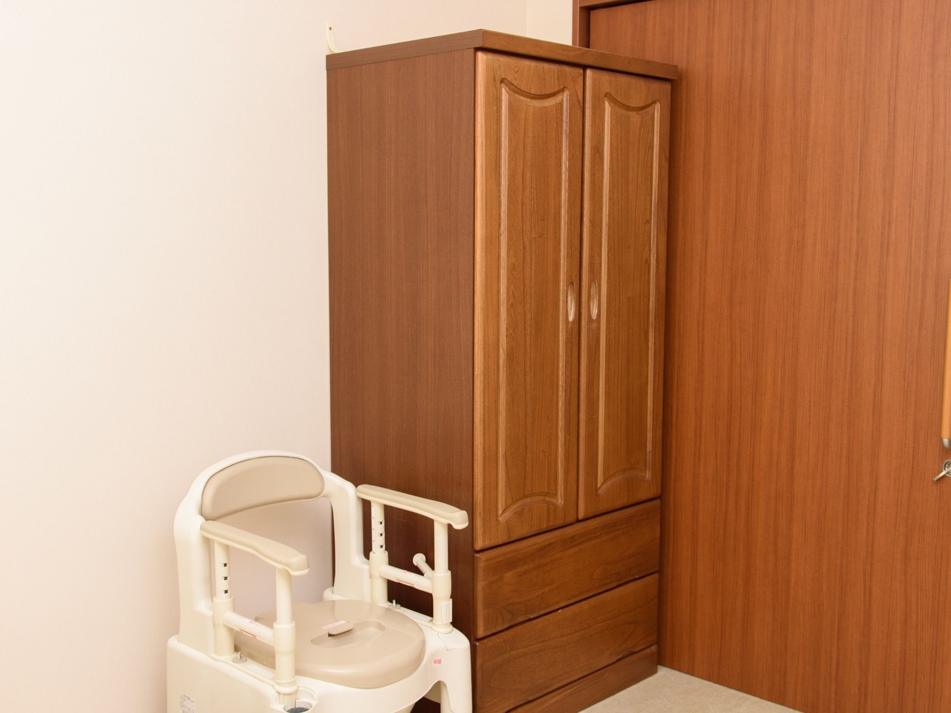 木目のドアのすぐ側に、木製の衣装ケースが置いてある。その左側には、ポータブルトイレが用意されている。