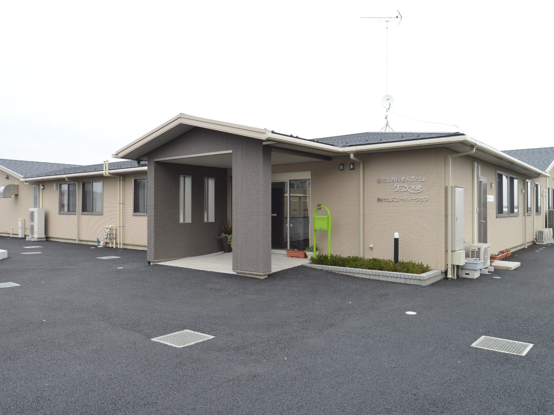 ゆるやかな勾配の先に自動ドアの玄関がある、平屋建ての施設外観